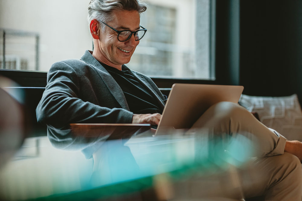 Older man seated on a couch working on a laptop