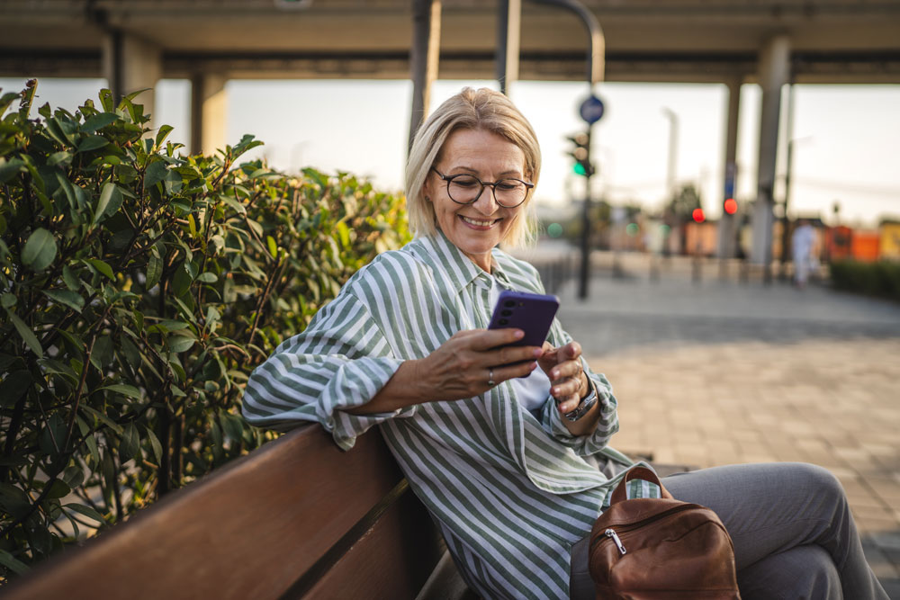 Older woman seated on a bench outside looking at her phone
